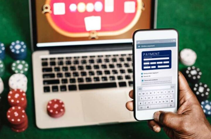 Person making an online payment on a smartphone with poker chips and a virtual casino table displayed on a laptop in the background.